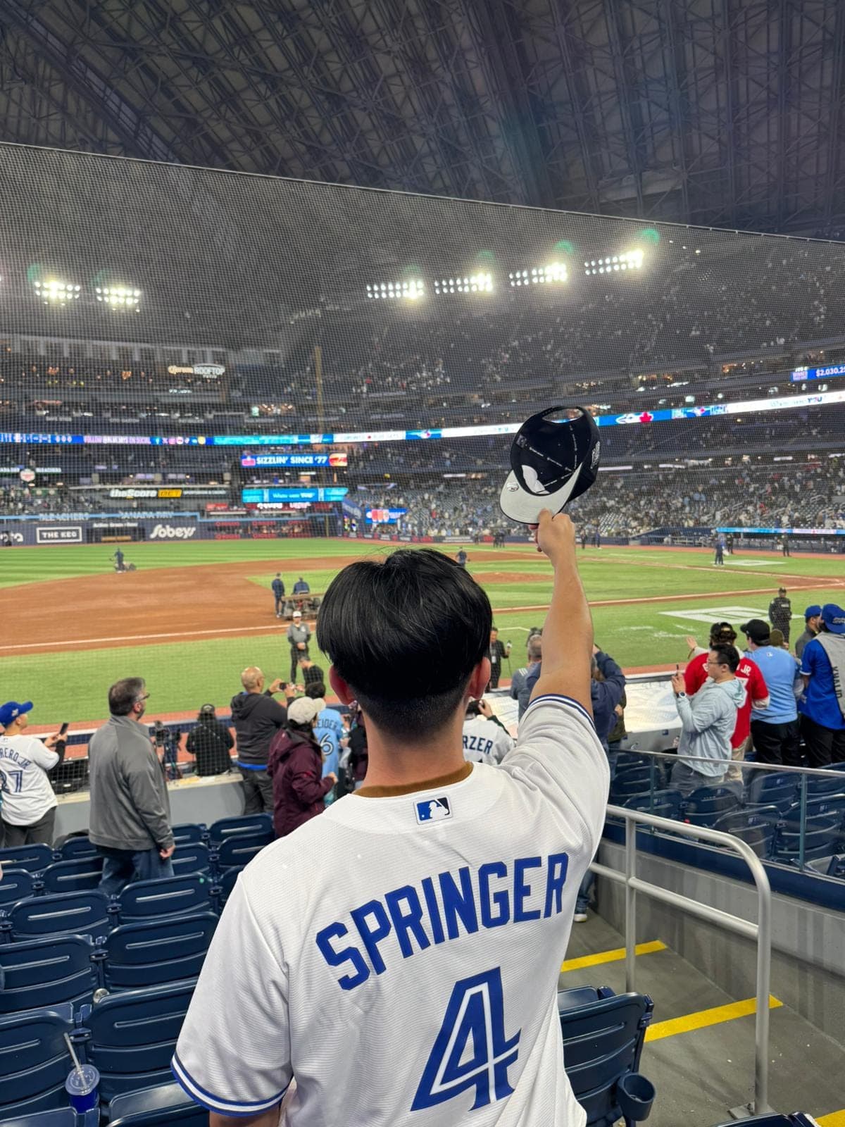 Suyu from behind in a Springer 4 jersey, holding a cap up toward the field at Rogers Centre