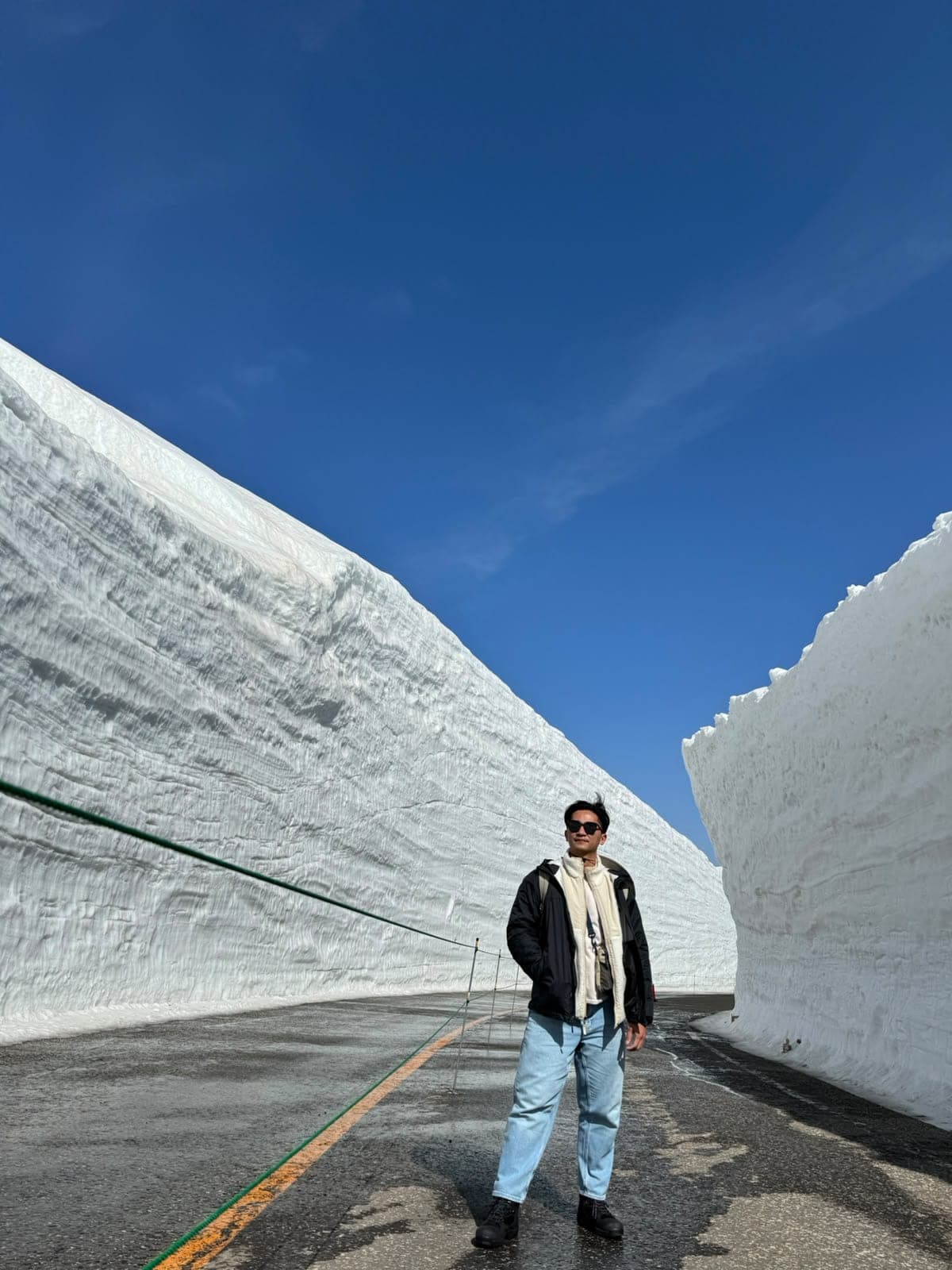 Suyu standing on a road between towering walls of snow under a clear blue sky