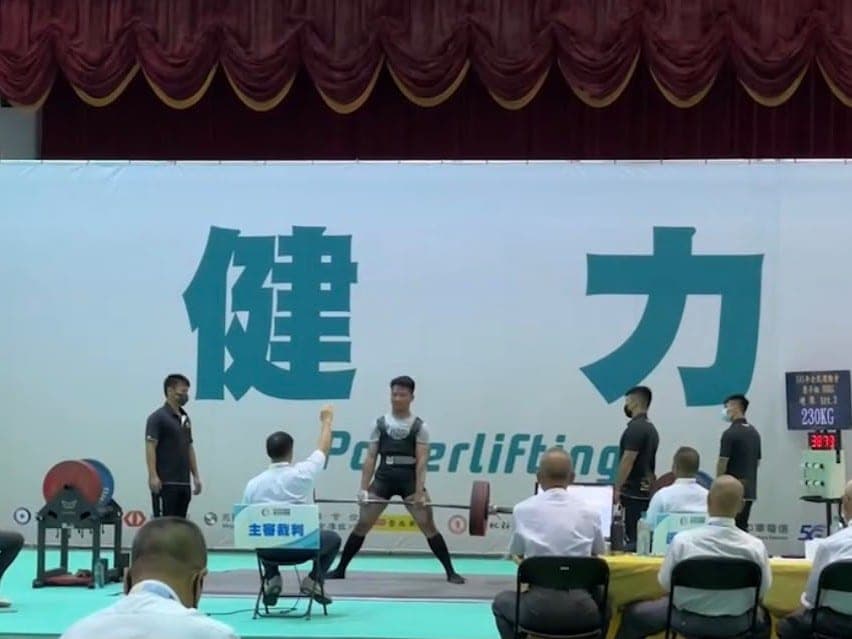 Suyu at the bar for a 230 kg deadlift on the competition platform, with referees watching